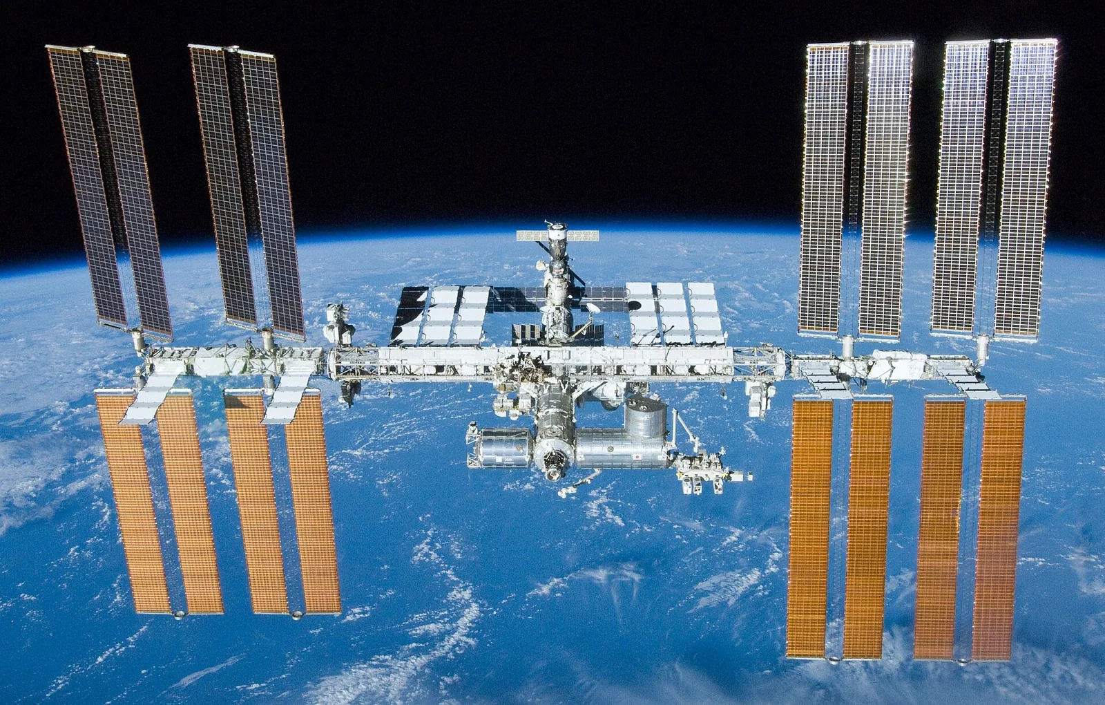 The International Space Station above the blue Earth: a long truss with white modules and eight large solar panels