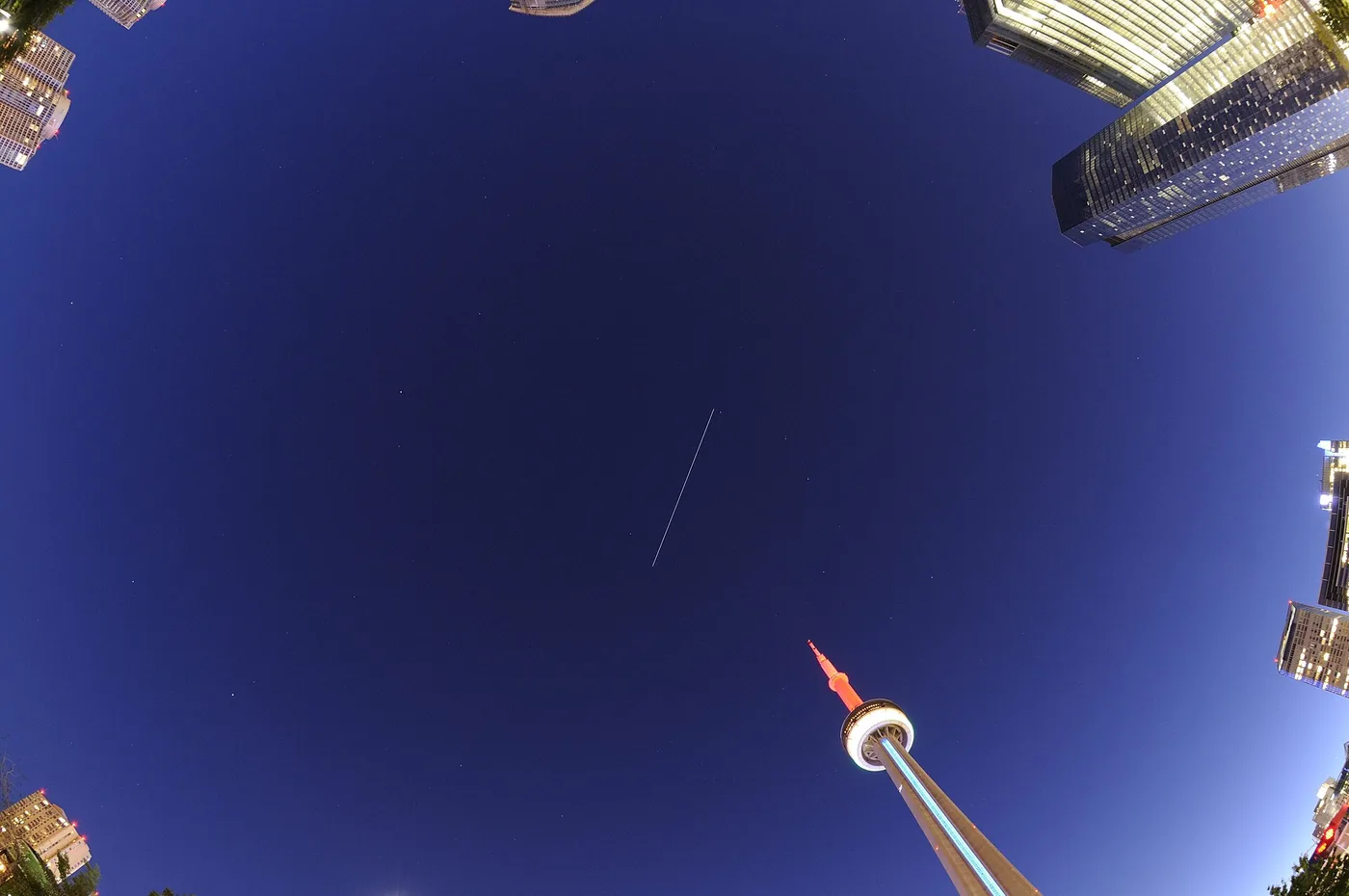 Dark blue sky above the lights of Toronto, with a thin white streak: the space station in a 15-second exposure