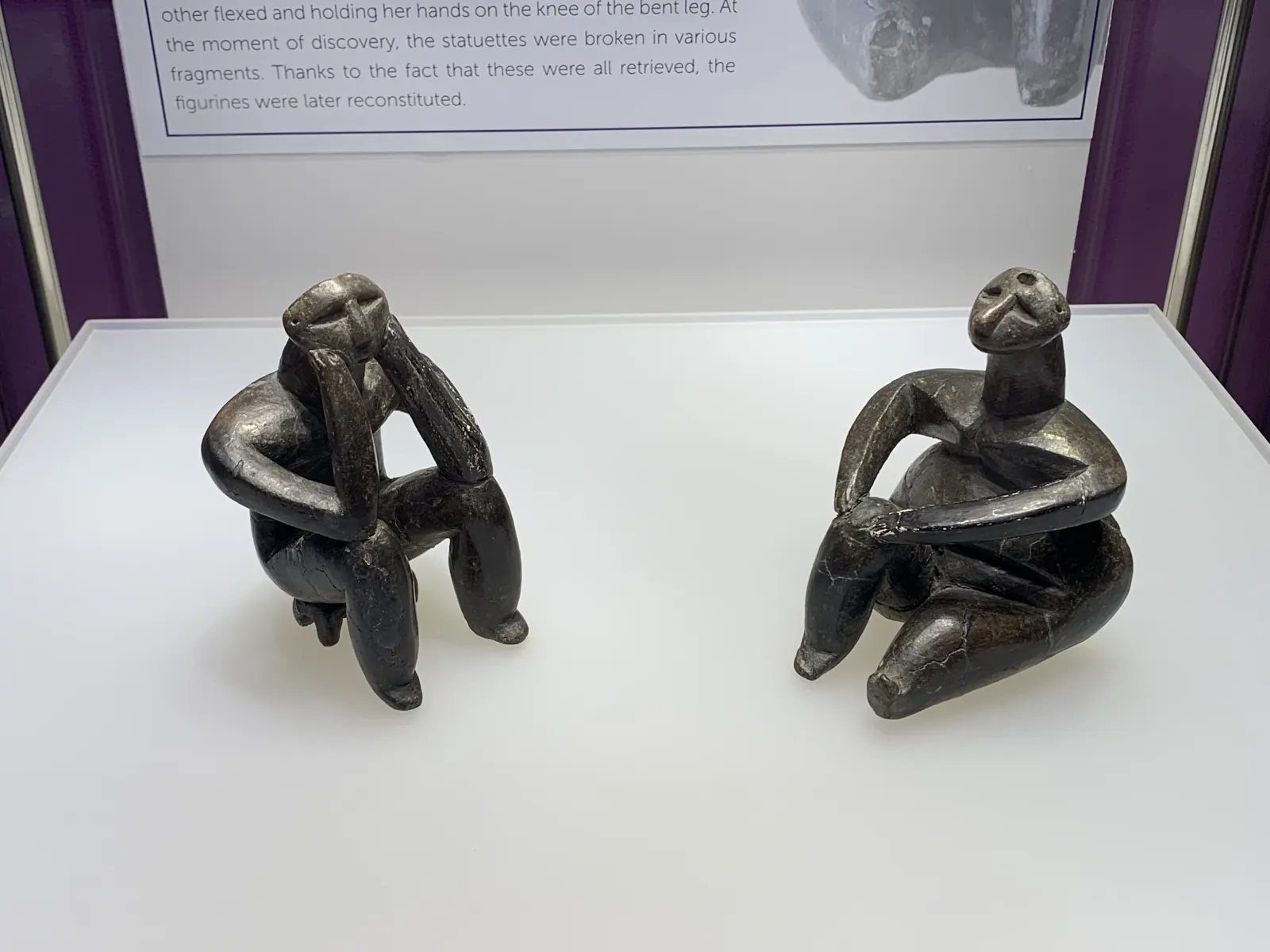 Două figurine șezând; cea din stânga își sprijină capul în mâini.