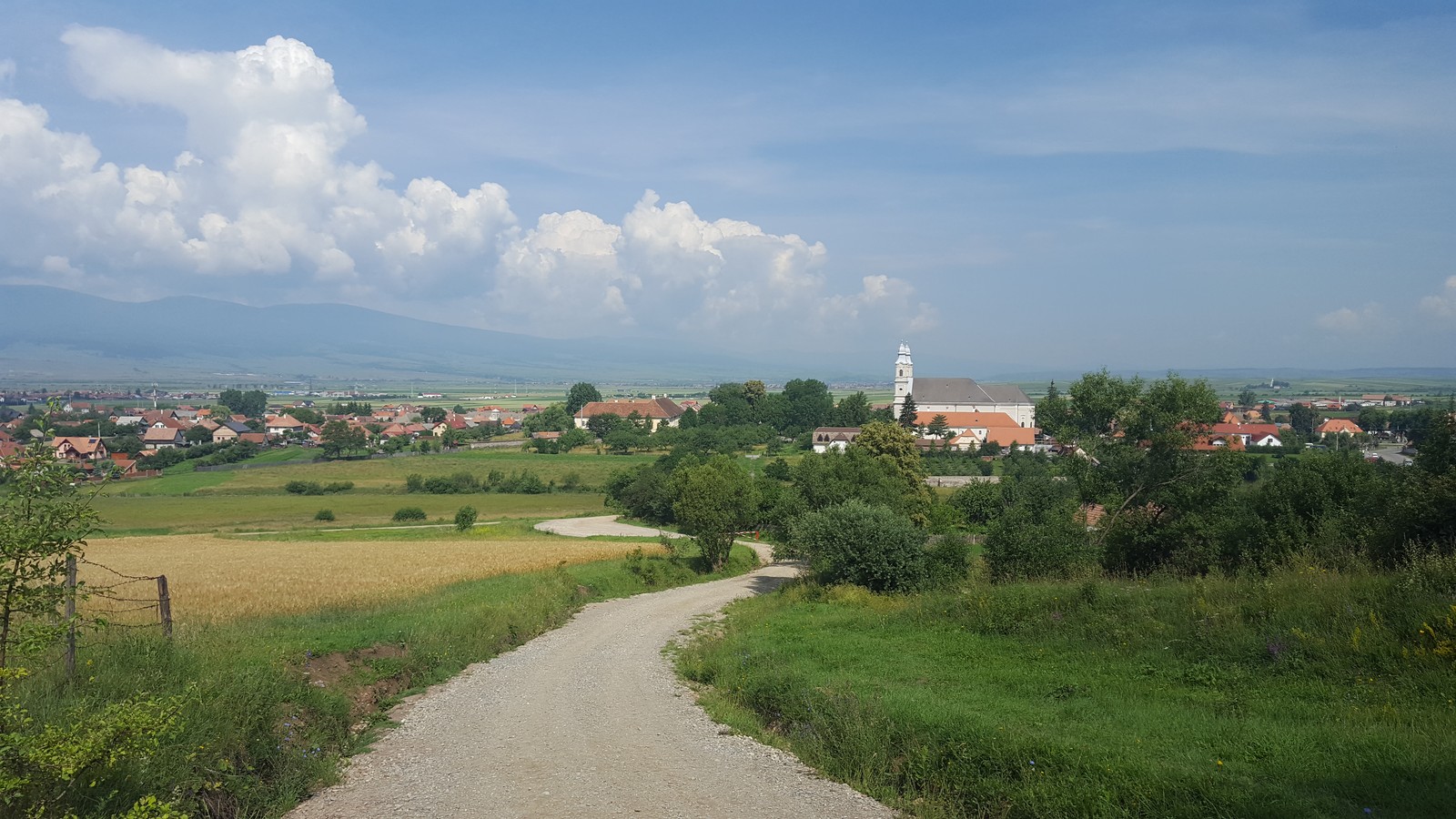 The dirt road running down to the Franciscan monastery at Șumuleu Ciuc (Csíksomlyó), seen from the hill on a summer day.