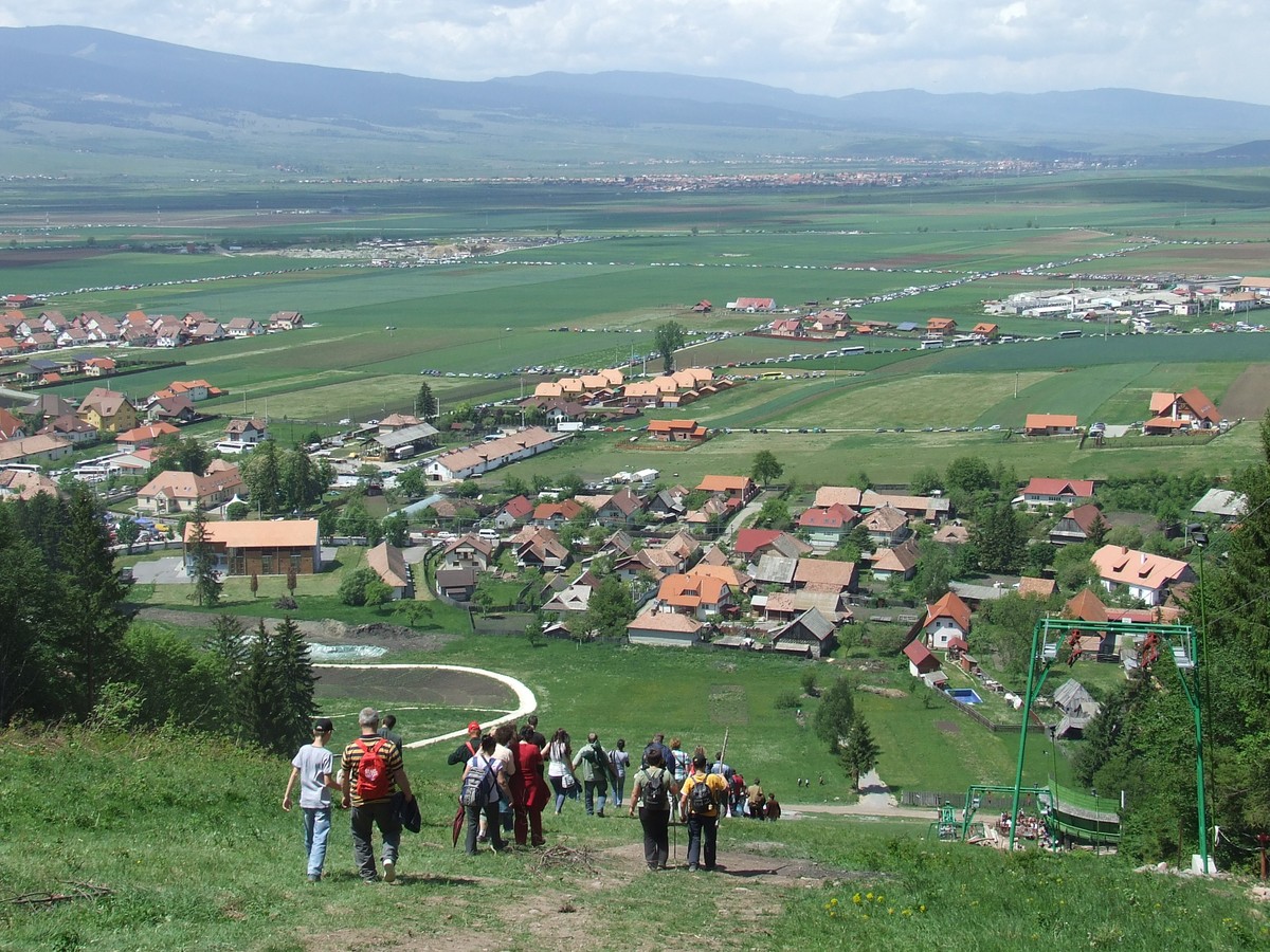 The valley below the Șumuleu saddle on feast day: tents, cars and pilgrims toward the horizon.