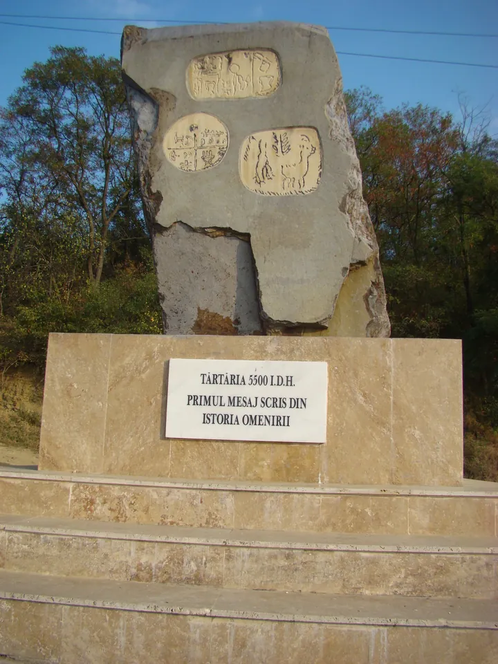 Lespezi de piatră cioplite cu semne vechi, înălțate ca monument pe un câmp verde, sub cer albastru.