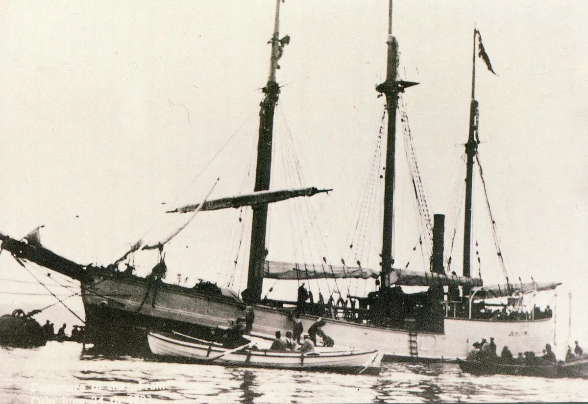 Old photograph of the three-masted ship Fram afloat with small boats alongside.