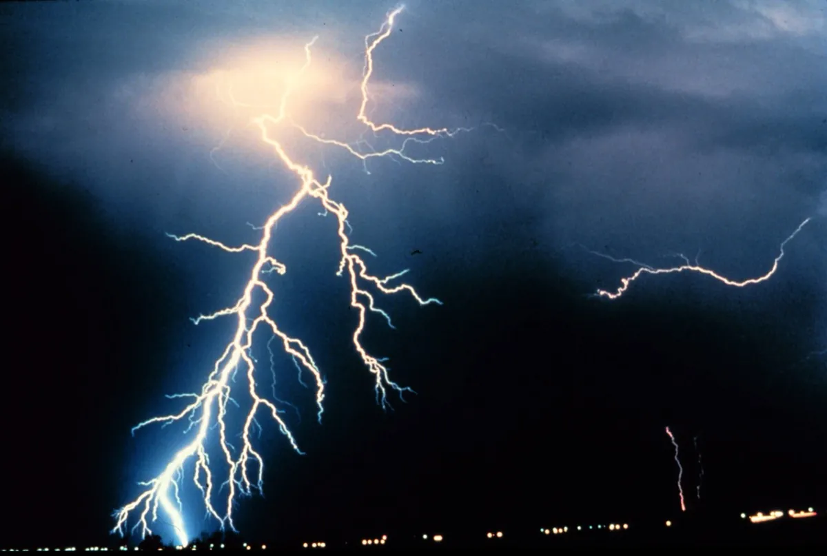Night thunderstorm with a branching cloud-to-ground lightning stroke and a second stroke at right.