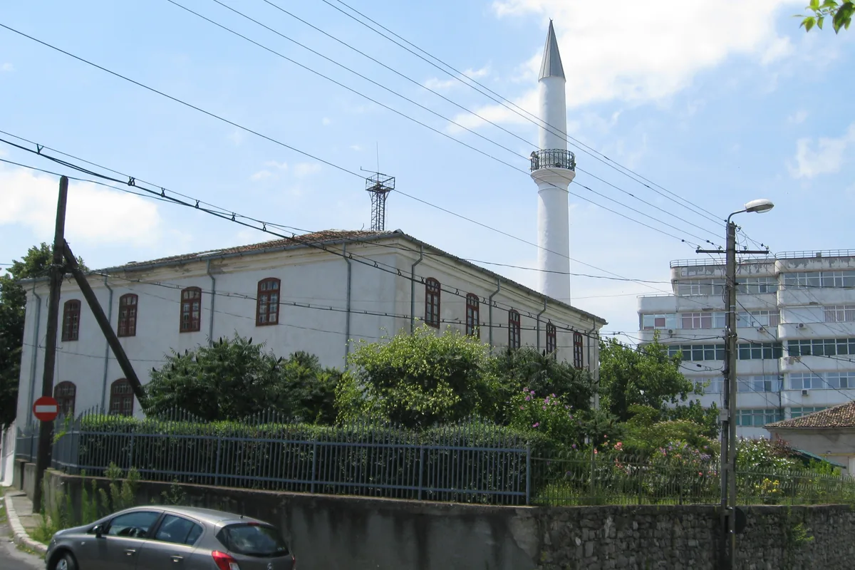 Zidul alb al geamiei Azizyie văzut din stradă, cu două rânduri de ferestre și minaretul în spate