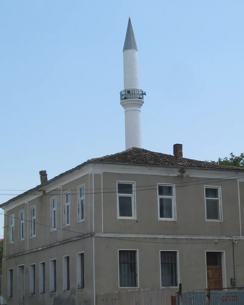Casa cu două caturi a fostei școli turcești, cu minaretul alb în spate