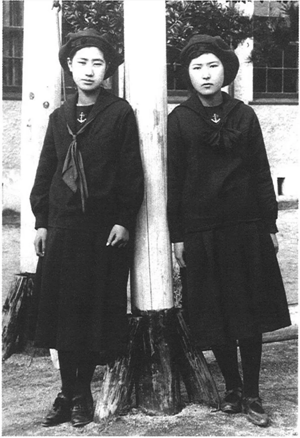 Două eleve ale școlii Fukuoka Jo Gakuin, anii 1920, în uniforme închise la culoare cu guler de marinar și ancoră brodată.