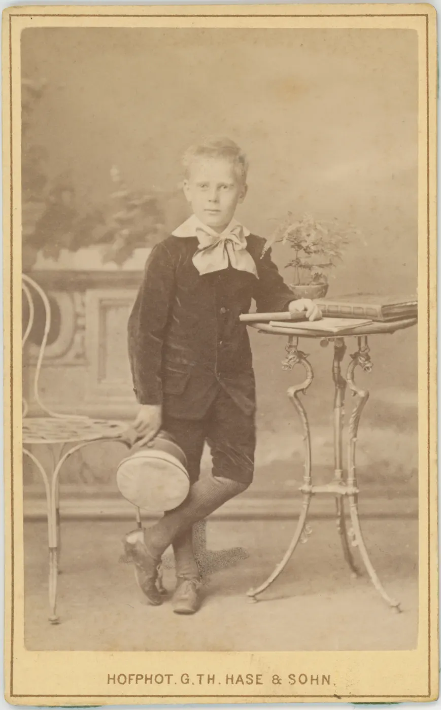Fotografie de atelier dintr-un oraș german, 1881: un băiat în costum ține în mână șapca de elev.
