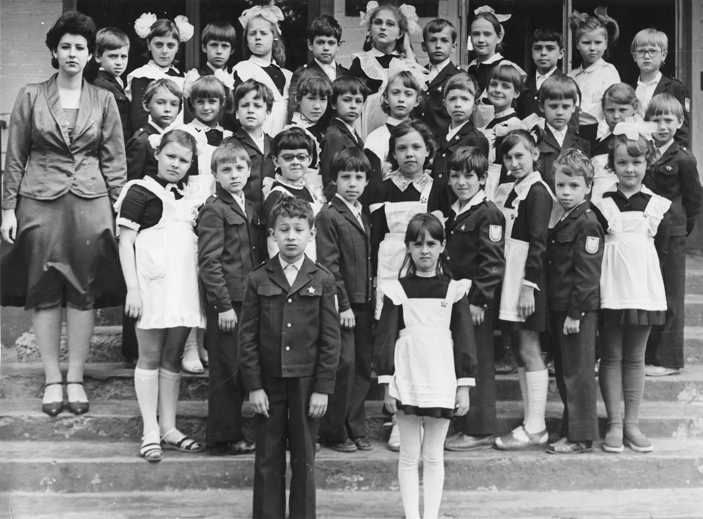 Fotografie de clasă alb-negru, Rostov-pe-Don, 1986: băieți în costume închise, fete în rochii cu șorțuri albe, pe treptele școlii.