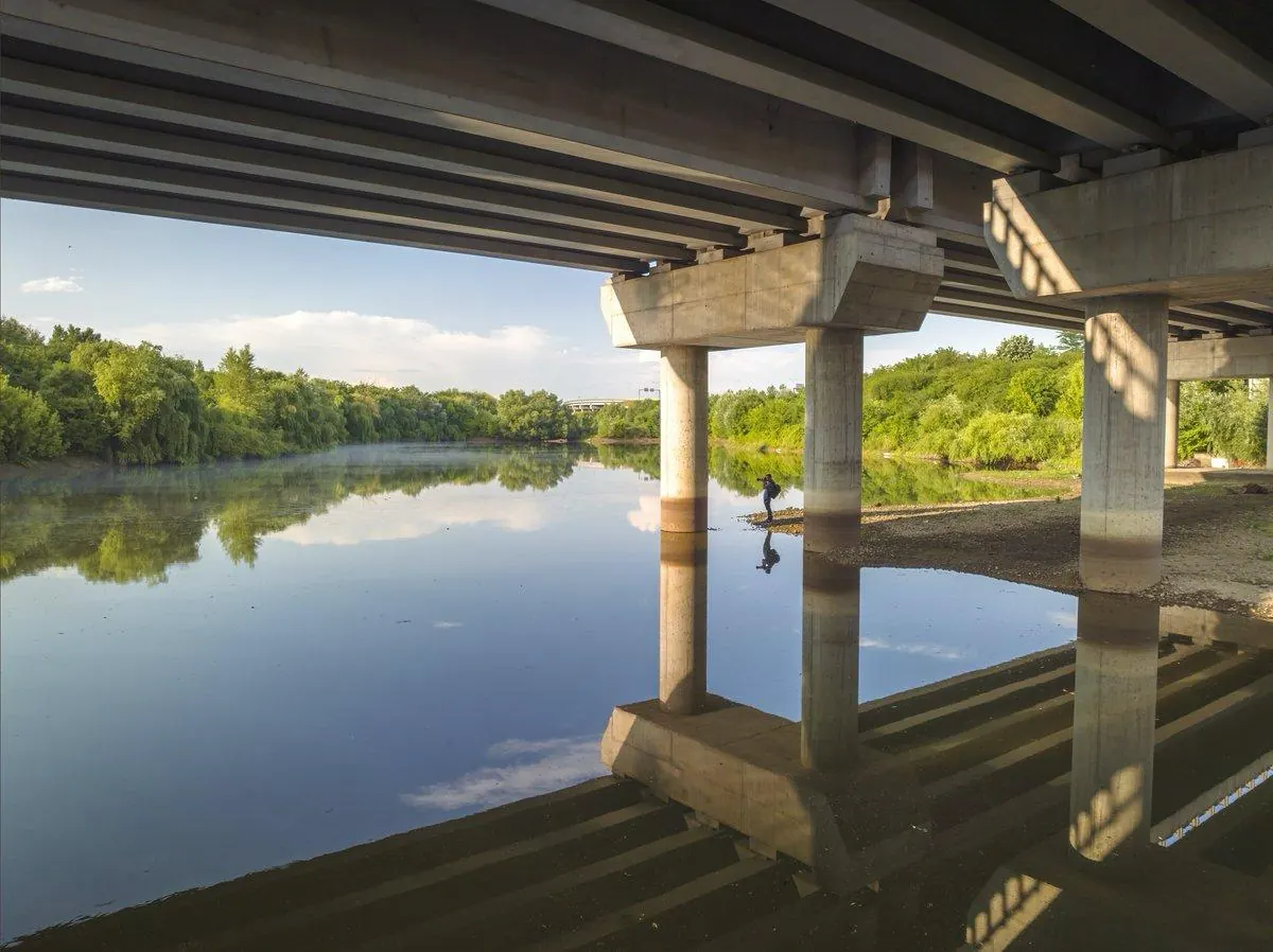 Concrete pillars of a motorway bridge over still water, with an angler and willows behind.
