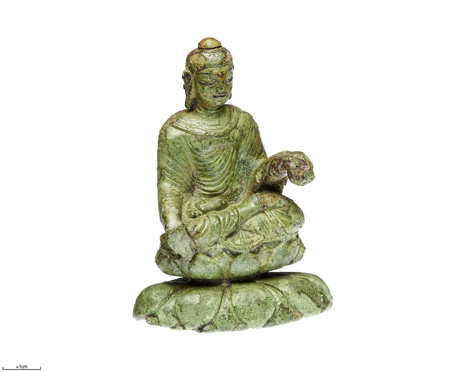 O mică statuetă de bronz verzui a lui Buddha așezat, pe un soclu de lotus, fotografiată pe fond alb.