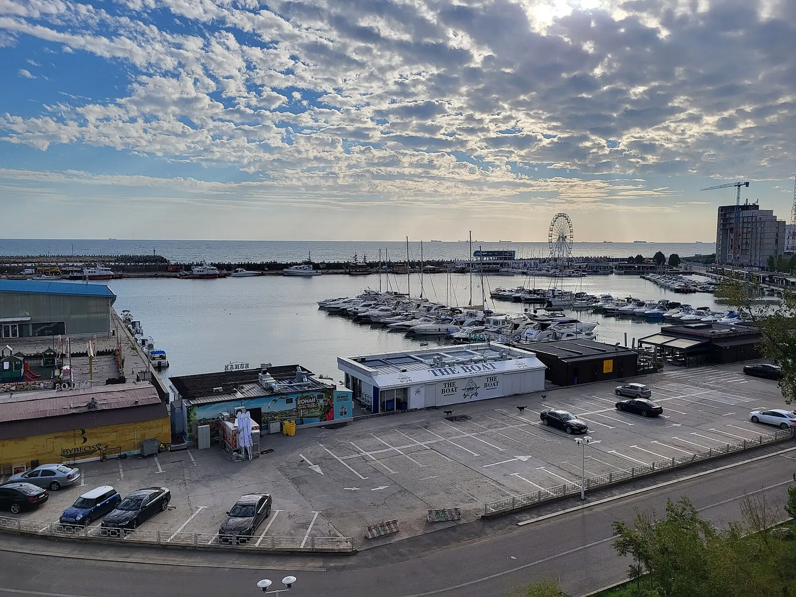 Vedere aeriană a unui port de agrement cu bărci acostate și un soare jos în spatele norilor risipiți, deasupra mării.