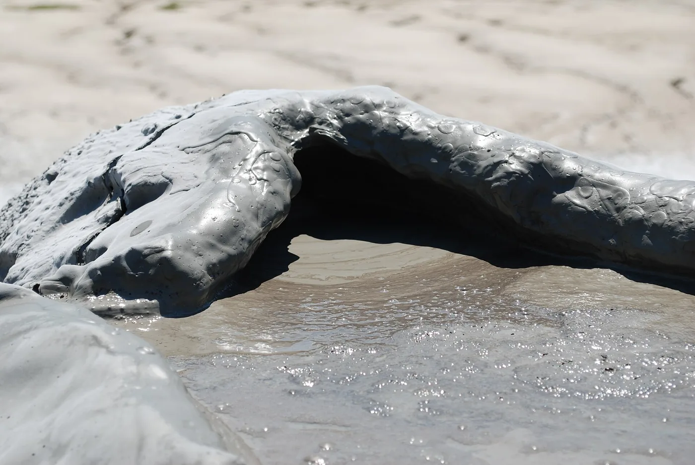 A mud crater close up: cracked grey walls and the round mouth the mud comes out of.